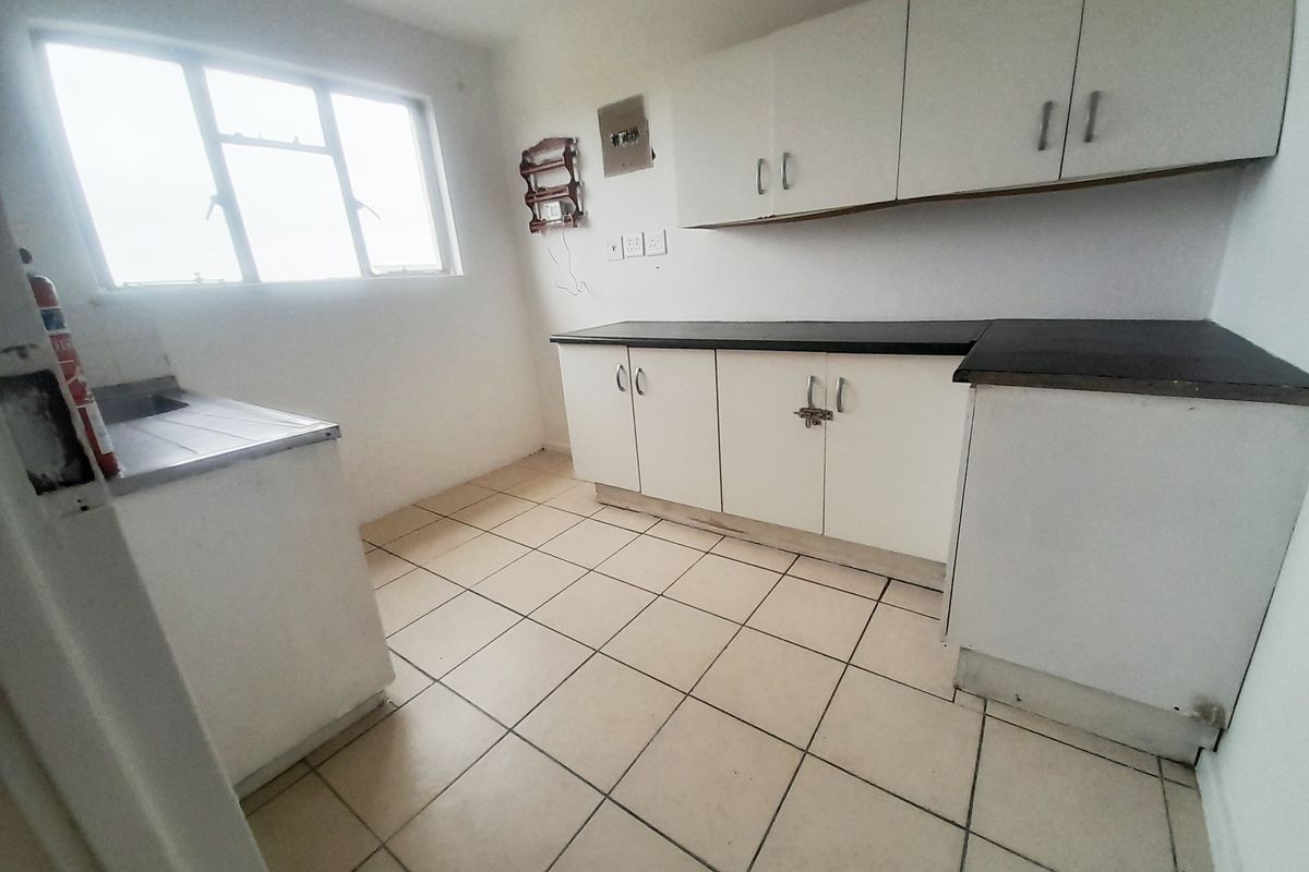 A functional kitchen space featuring white cabinetry, dark countertops, and tiled flooring, offering a blank canvas for potential updates and modernization.