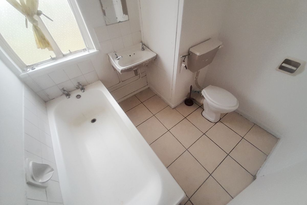 A dated bathroom featuring a standard bathtub, wall-mounted basin, and toilet with tiled flooring and splashbacks.