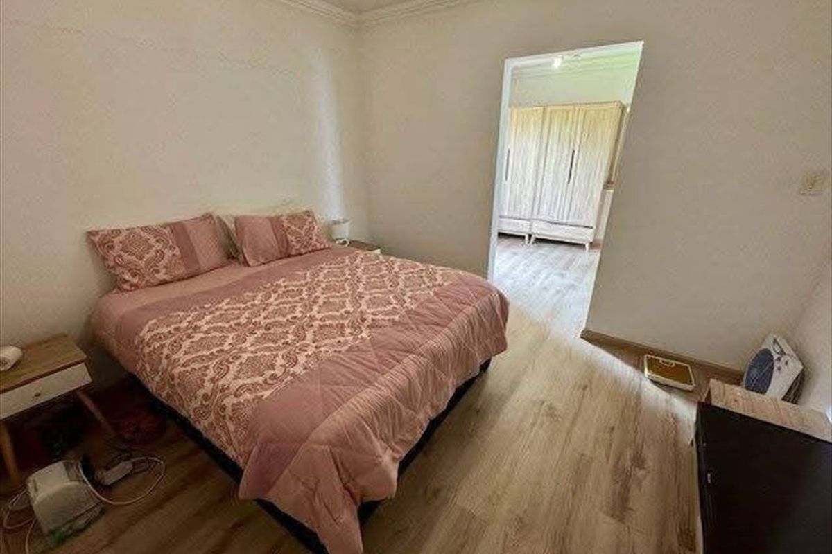 A bedroom featuring light wood-look flooring and crown molding, with an adjacent room visible through the doorway containing built-in cabinetry.