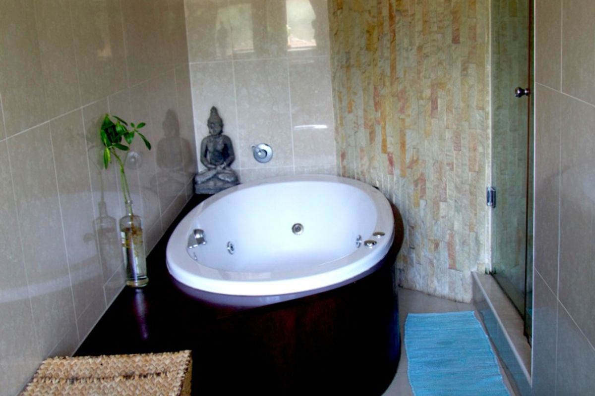 Modern bathroom featuring a built-in corner jetted bathtub with dark wood surround and a textured stone feature wall, adjacent to a glass-enclosed shower.