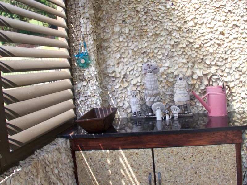 A unique outdoor utility area featuring custom shell-encrusted wall finishes, a dark stone countertop, and built-in cabinetry with louvered window shutters.