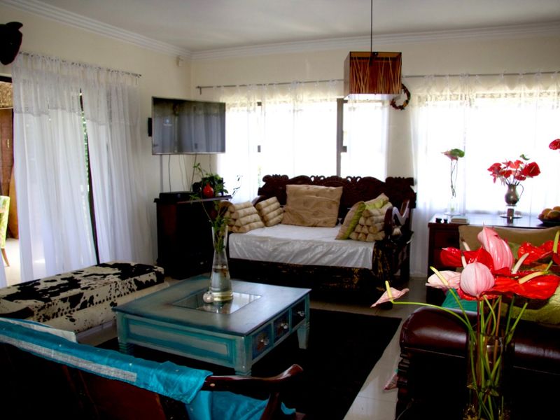A comfortable living room featuring large windows with natural light, tiled flooring, and a wall-mounted television setup.