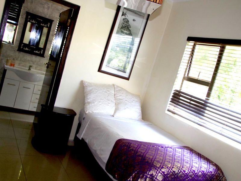 A bedroom featuring tiled flooring, a window with fitted blinds, and an en-suite bathroom with a vanity basin.
