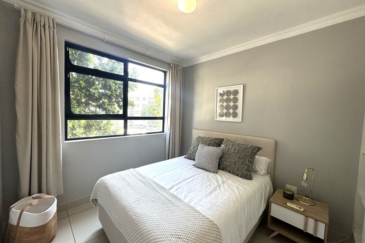 A well-maintained bedroom featuring neutral wall tones, tiled flooring, and a large window providing natural light.