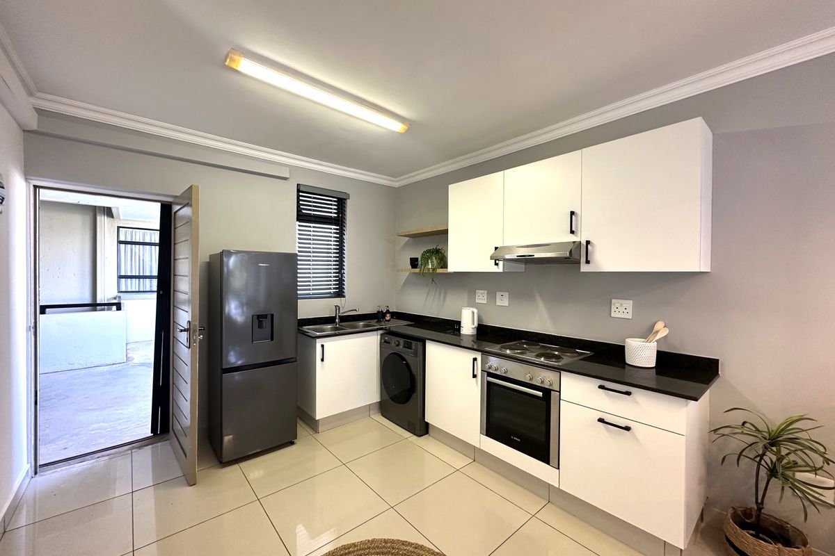 Modern kitchen featuring white cabinetry, black stone countertops, built-in oven, hob, extractor fan, and tiled flooring with direct access to an outdoor balcony.