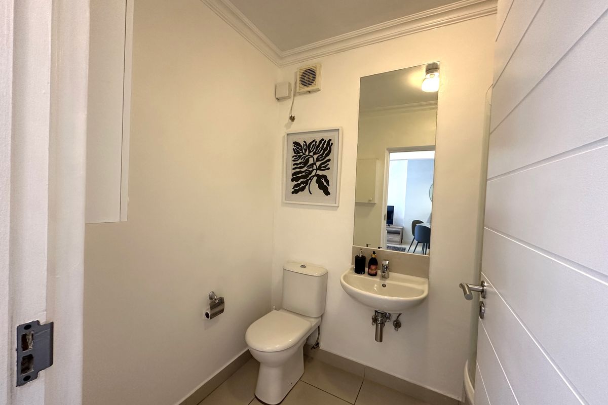 A compact guest bathroom featuring a wall-mounted basin, a standard toilet, and a wall-mounted mirror.