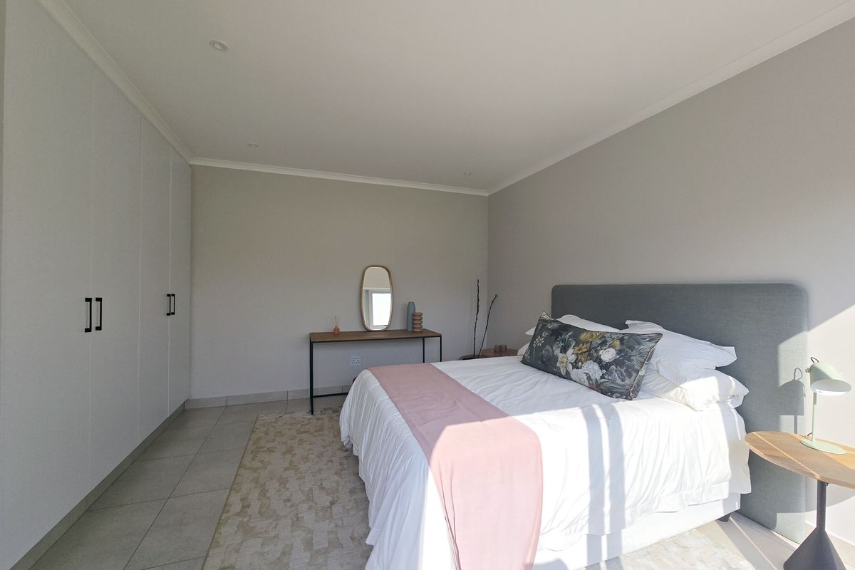 A bright and modern bedroom featuring neutral walls, tiled flooring, and extensive built-in floor-to-ceiling cabinetry for ample storage.