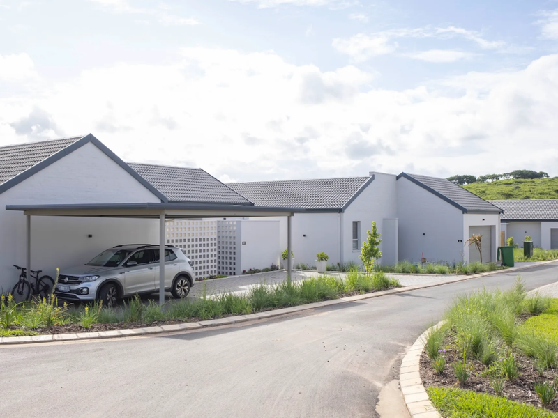 A modern residential street view featuring white facades, tiled roofs, and a convenient carport, set within a well-maintained estate environment.