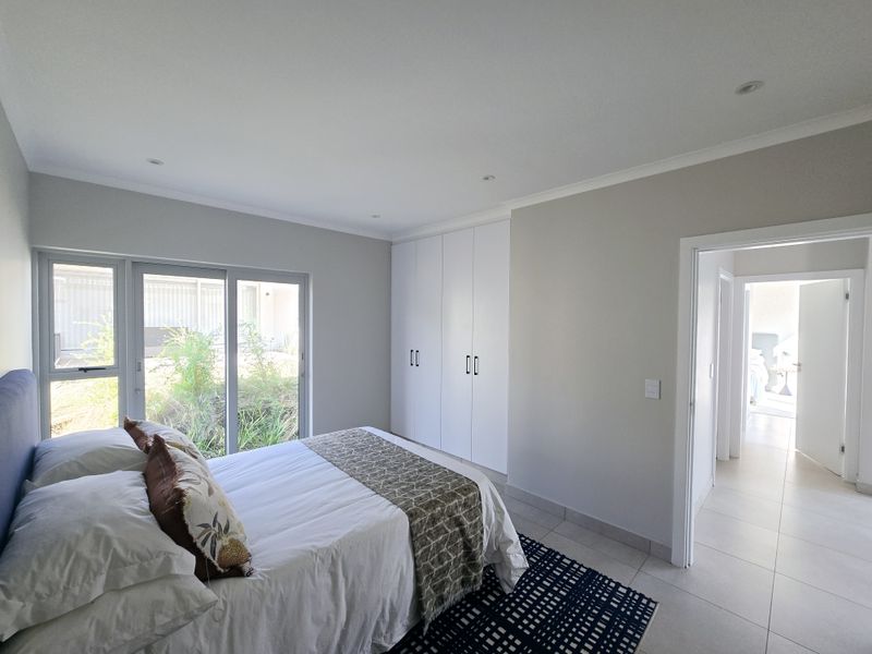 A bright bedroom featuring built-in wardrobes, tiled flooring, and large sliding glass doors providing natural light and garden access.