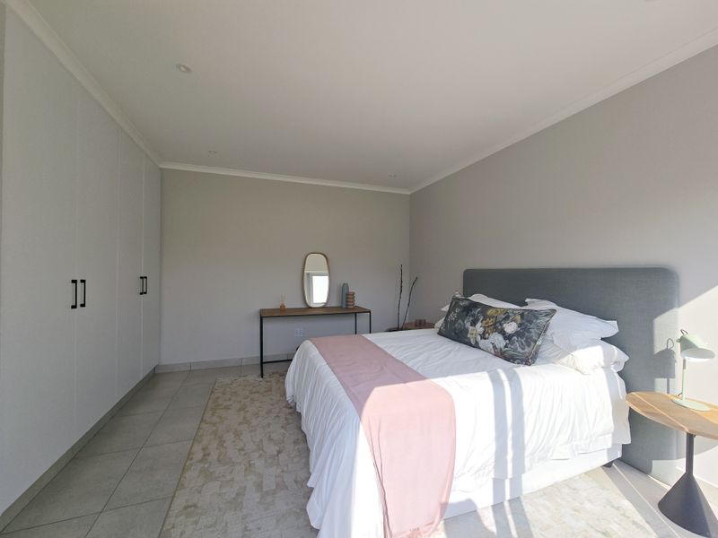 A bright and modern bedroom featuring neutral walls, tiled flooring, and extensive built-in floor-to-ceiling cabinetry for ample storage.