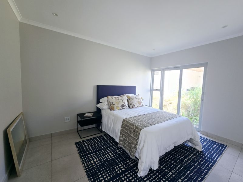 A bright bedroom featuring neutral tiled flooring, recessed ceiling lighting, and large sliding glass doors providing direct access to the outdoor area.