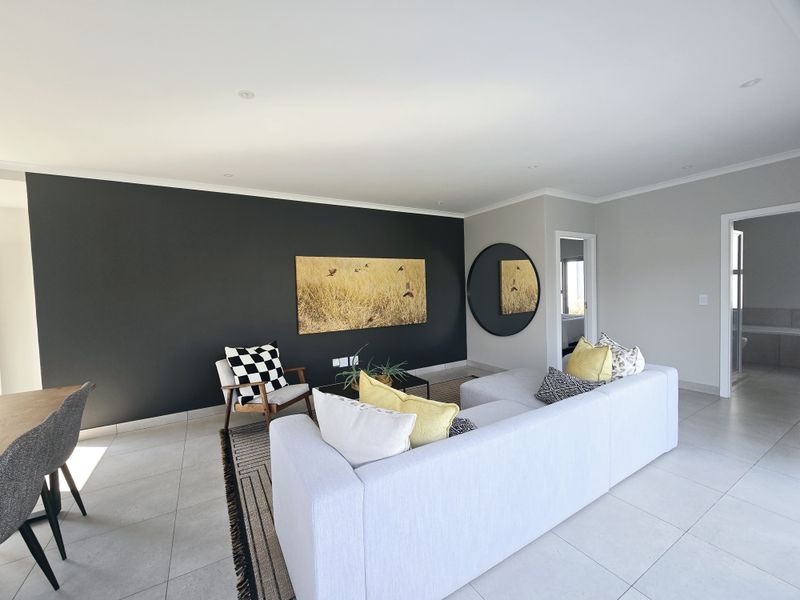 A bright and modern living area featuring large format floor tiles, recessed downlighting, and a striking dark feature wall.