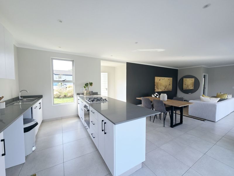 Modern open-plan kitchen and dining area featuring sleek white cabinetry, stone countertops, a central island with a gas hob, and large format floor tiles.