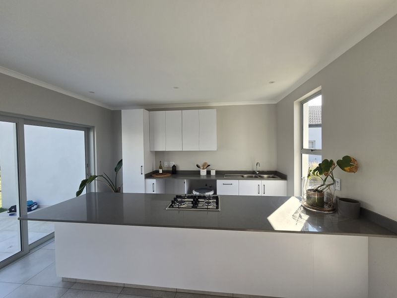 Modern kitchen featuring a central island with a built-in gas hob, sleek white cabinetry, stone countertops, and direct access to an outdoor patio area.