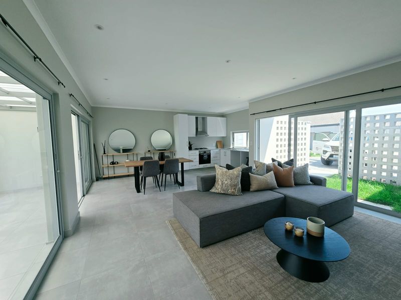 Modern open-plan living area featuring a sleek kitchen with built-in appliances, tiled floors, and large sliding glass doors providing seamless indoor-outdoor flow.
