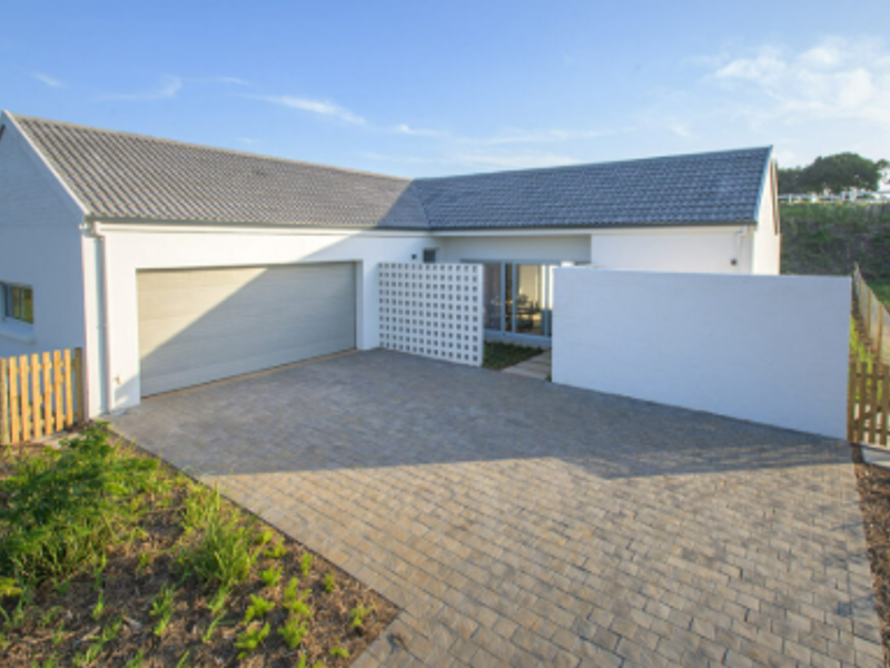 Modern single-story home exterior featuring a paved driveway, double garage, and clean white facade with decorative screen wall.
