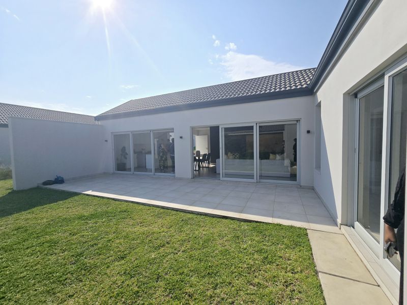 A modern rear exterior view featuring a tiled patio area, large sliding glass doors, and a well-maintained lawn.