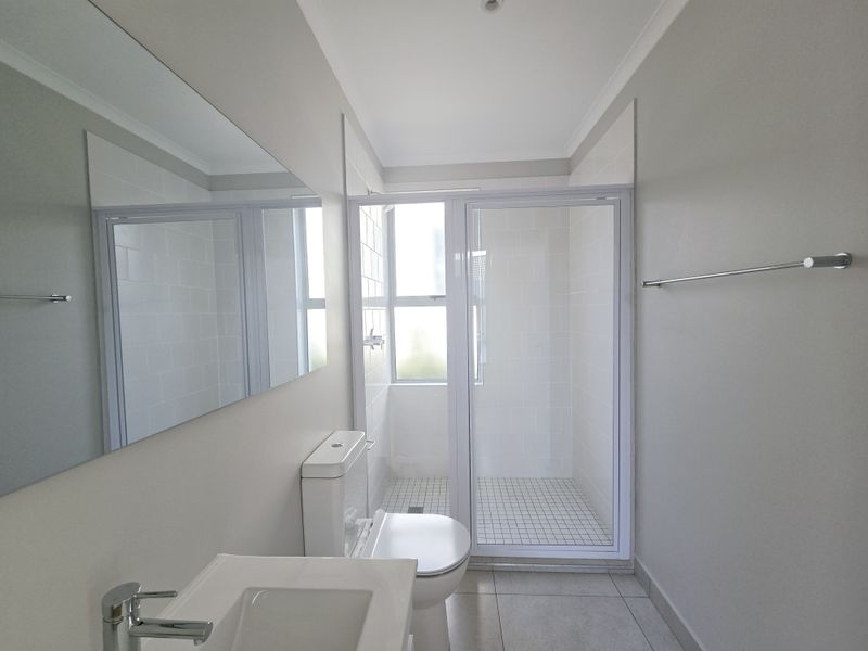 A clean and modern bathroom featuring a walk-in shower with white tiling, a wall-mounted mirror, and a contemporary vanity basin.