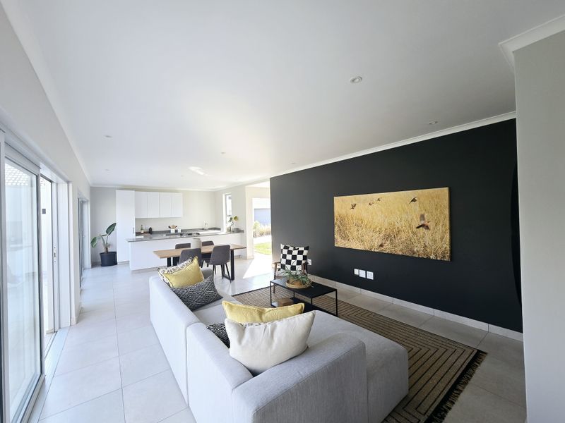 Modern open-plan living area featuring a sleek kitchen with white cabinetry, tiled flooring, and a striking black feature wall.