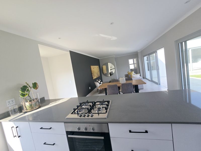 Open-plan living area featuring a modern kitchen with stone countertops, built-in gas hob, and oven, flowing seamlessly into the dining and lounge space.