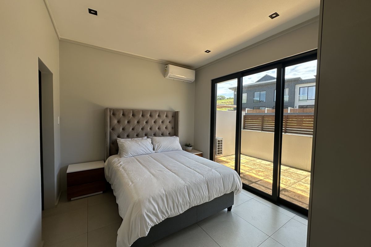 A modern bedroom featuring tiled flooring, recessed ceiling lighting, a wall-mounted air conditioning unit, and large sliding glass doors leading to a private balcony.