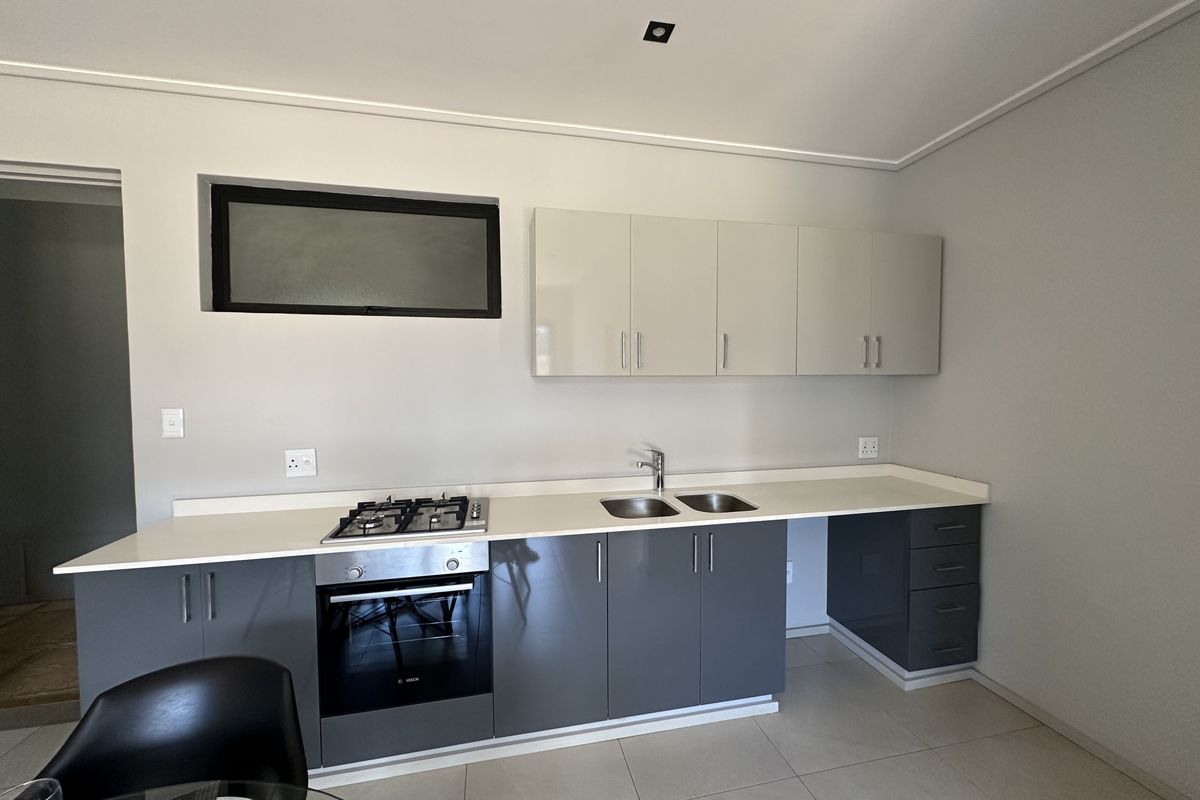 Modern kitchen featuring sleek grey and white cabinetry, stone countertops, a built-in gas hob, oven, and double stainless steel sink.