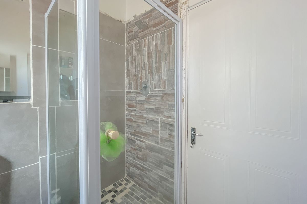 Bathroom featuring a glass-enclosed shower with textured stone-look wall tiles and mosaic floor tiling, requiring finishing touches around the door and wall edges.