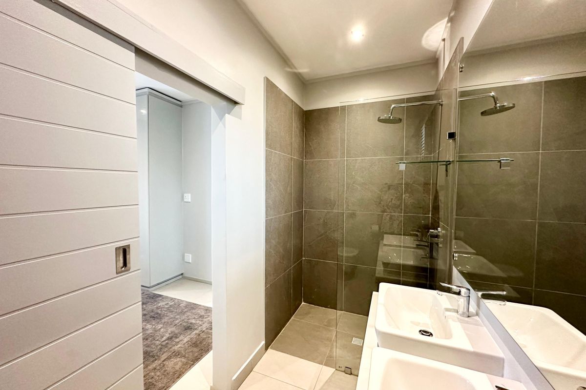 Modern bathroom featuring a double vanity, large wall-mounted mirror, and a spacious walk-in shower with glass enclosure and sliding door access.
