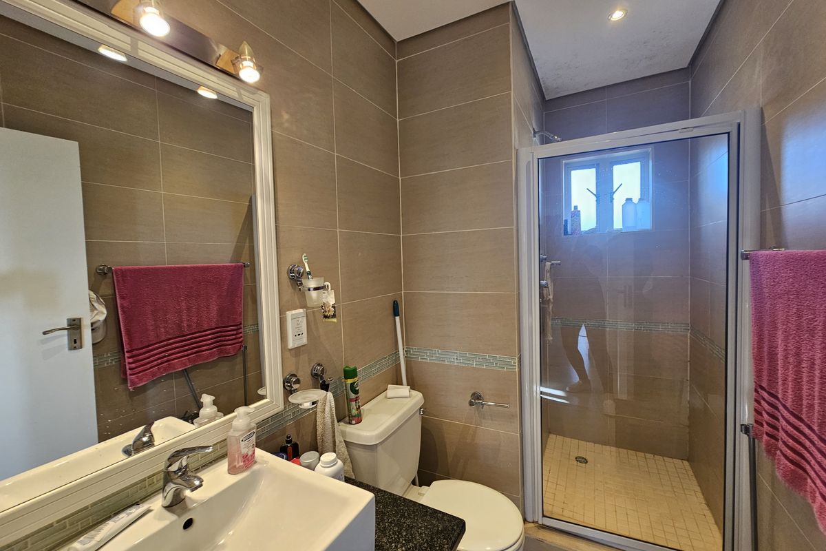 A functional bathroom featuring a glass-enclosed shower, vanity with basin, wall-mounted mirror, and neutral wall tiling.