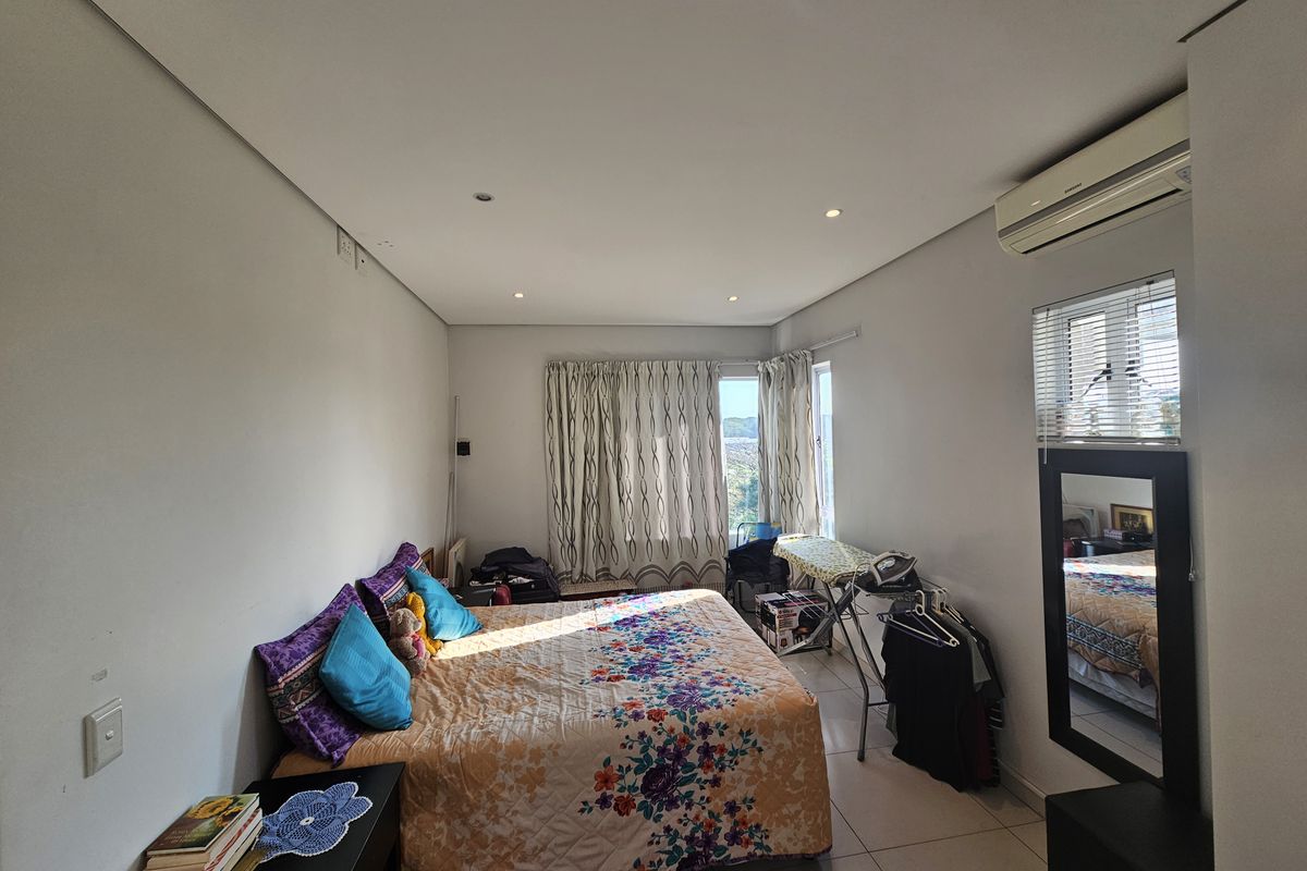 A bedroom featuring tiled flooring, recessed ceiling lighting, and a wall-mounted air conditioning unit, with natural light entering through a window.