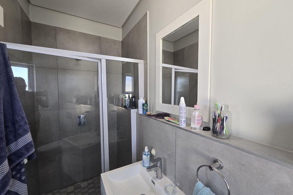 Modern bathroom featuring a glass-enclosed shower with grey wall tiles, a wall-mounted basin with chrome faucet, and a built-in vanity shelf.
