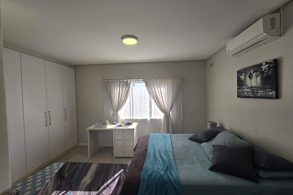 A well-maintained bedroom featuring built-in cupboards, a wall-mounted air conditioning unit, and tiled flooring with natural light from the window.