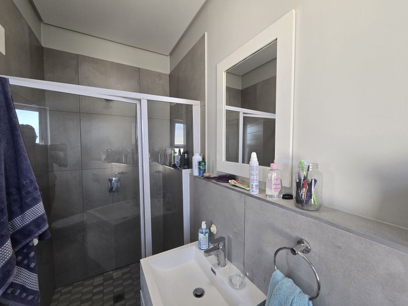 Modern bathroom featuring a glass-enclosed shower with grey wall tiles, a wall-mounted basin with chrome faucet, and a built-in vanity shelf.