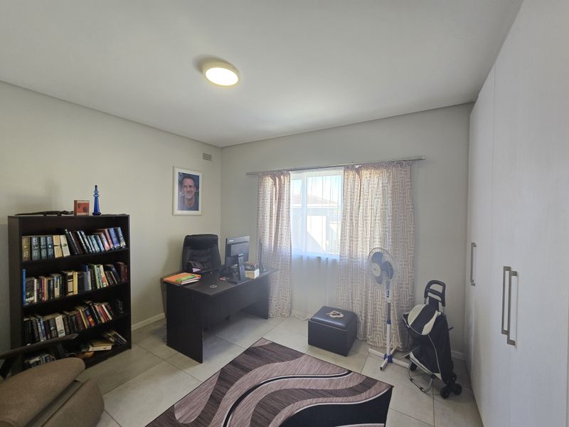 A functional home office featuring built-in cupboards, tiled flooring, and a window with curtain treatments, providing a practical workspace.