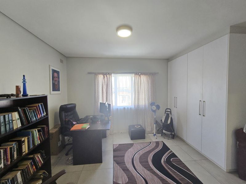 A functional bedroom featuring built-in floor-to-ceiling wardrobes, tiled flooring, and a window providing natural light.