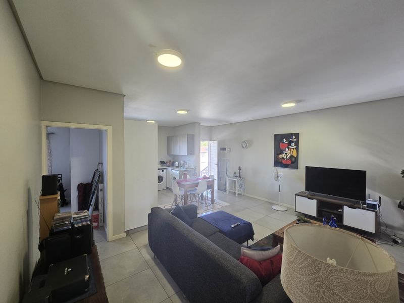 An open-plan living and kitchen area featuring tiled flooring, neutral walls, and recessed ceiling lighting, creating a functional and connected living space.