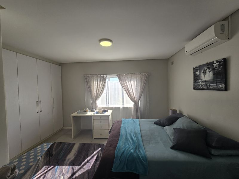 A well-maintained bedroom featuring built-in cupboards, a wall-mounted air conditioning unit, and tiled flooring with natural light from the window.