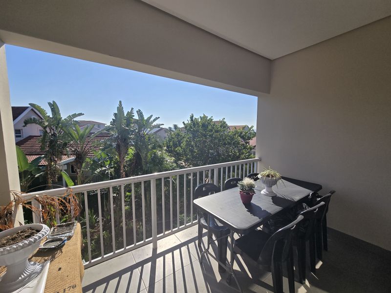 A covered balcony featuring tiled flooring and a white metal balustrade, offering an open view of the surrounding residential area and greenery.