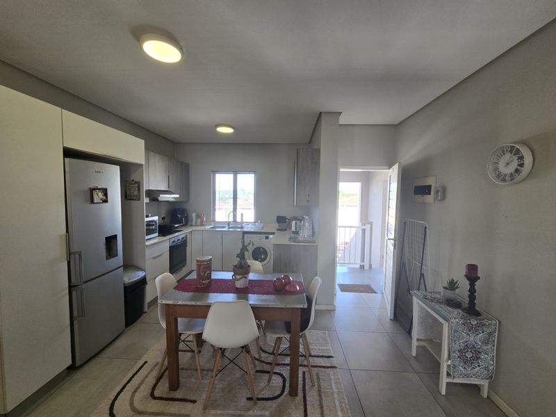 Open-plan kitchen and dining area featuring modern cabinetry, built-in oven, hob, extractor fan, and tiled flooring with direct access to an outdoor balcony.