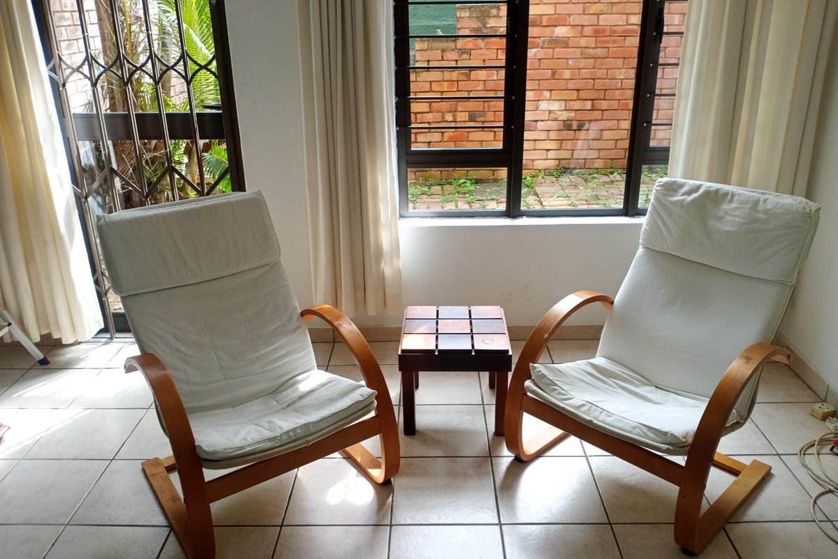 A bright living area featuring ceramic floor tiles, large windows with security bars, and access to an outdoor space.