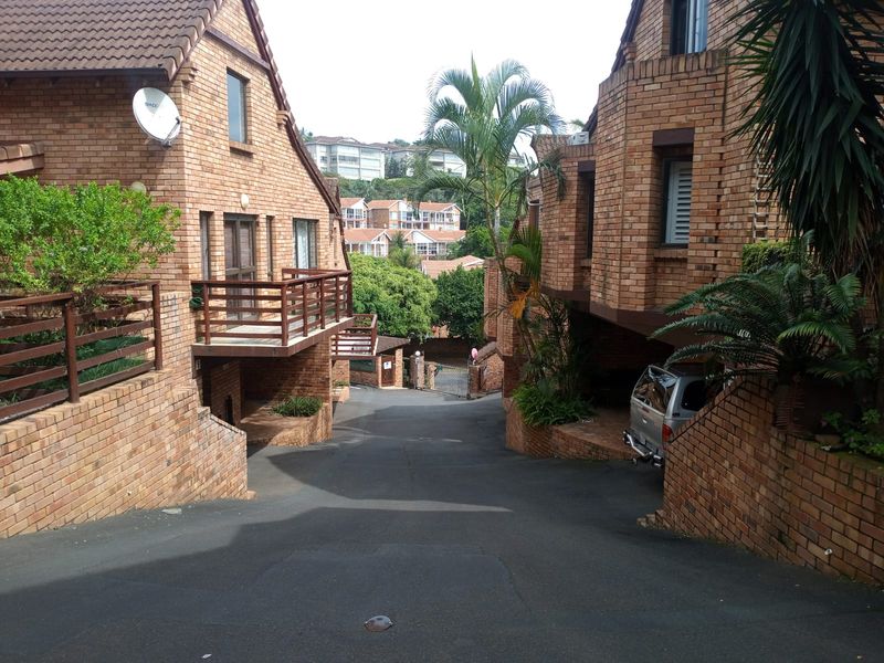 A view of the complex driveway and exterior brick facades of the apartment units, featuring balconies and established landscaping.