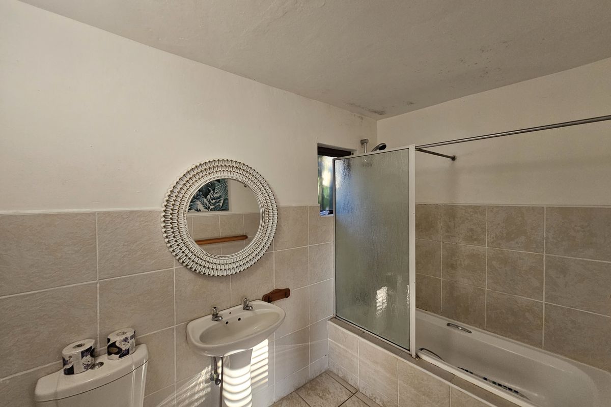 A functional bathroom featuring a pedestal sink, a bathtub with a glass shower screen, and neutral wall and floor tiling.