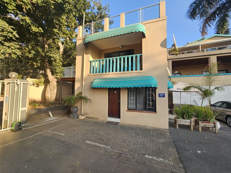 Front elevation of a multi-level apartment unit featuring a paved driveway, balcony with balustrade, and retractable fabric awnings.