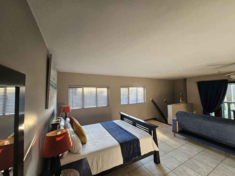 Spacious open-plan bedroom and living area featuring tiled flooring, large windows with fitted blinds, and direct access to an outdoor balcony.