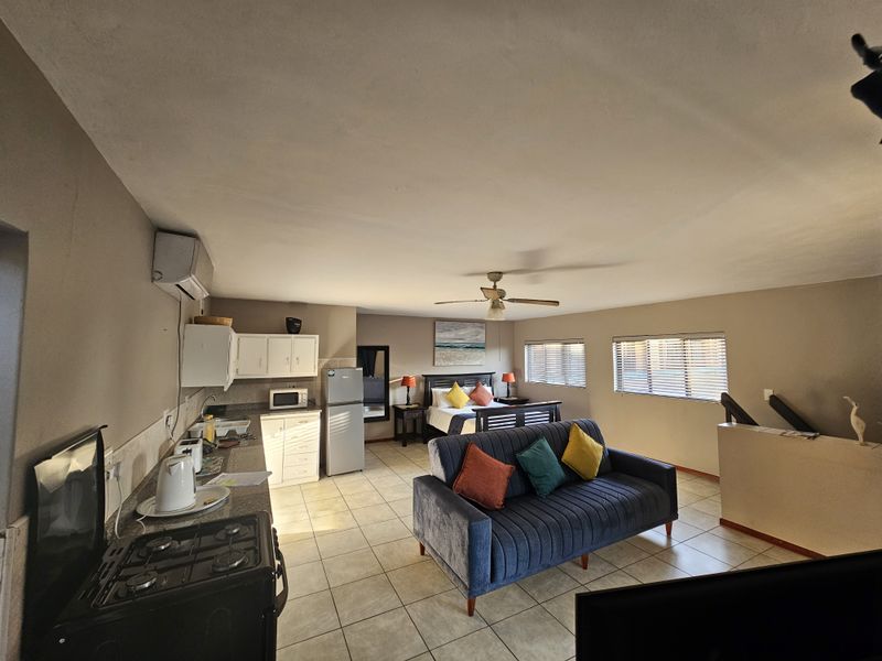 An open-plan studio apartment featuring a compact kitchenette with built-in cabinetry, tiled flooring, and a combined living and sleeping area.