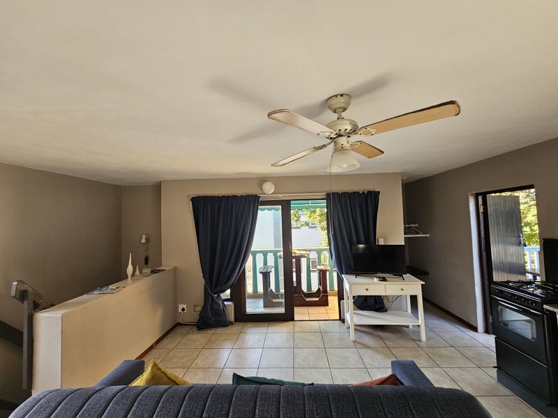 Open plan living area featuring tiled flooring, a ceiling fan, and direct access to a balcony through sliding glass doors.