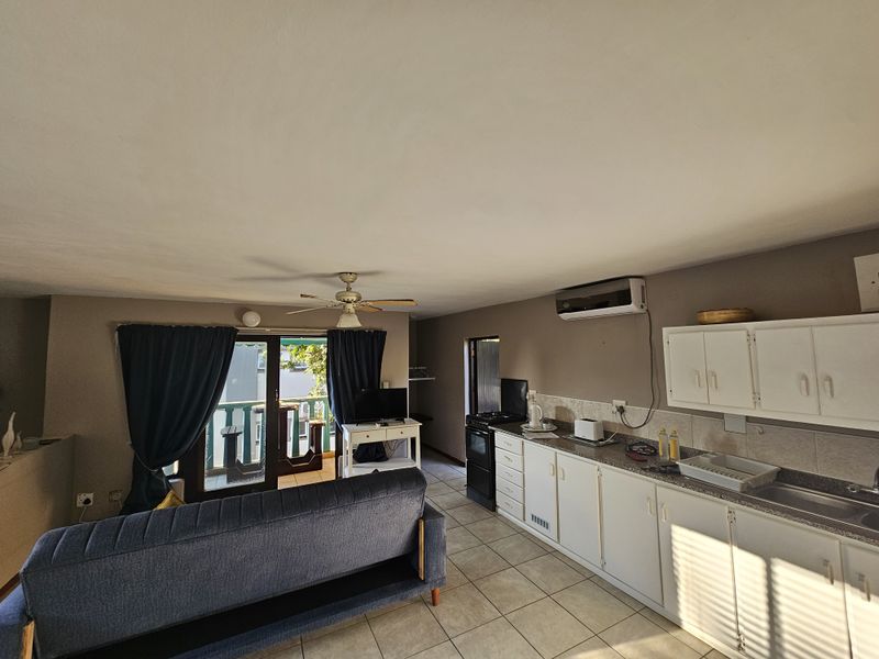 Open-plan living area featuring a functional kitchen with white cabinetry, tiled flooring, ceiling fan, and direct access to a private balcony.