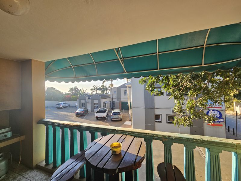 A covered balcony area featuring a built-in braai and a green awning, overlooking the apartment complex parking area.