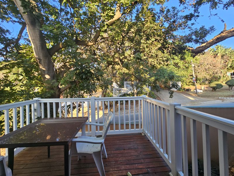 A wooden balcony deck featuring white balustrades, overlooking a leafy residential street with mature trees.