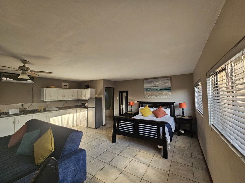 Open-plan studio apartment featuring a compact kitchen with white cabinetry, tiled flooring, and a combined living and sleeping area with ceiling fan.